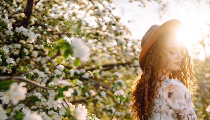 a girl in a hat walking trough the tree blossoms that are full of white blossoms